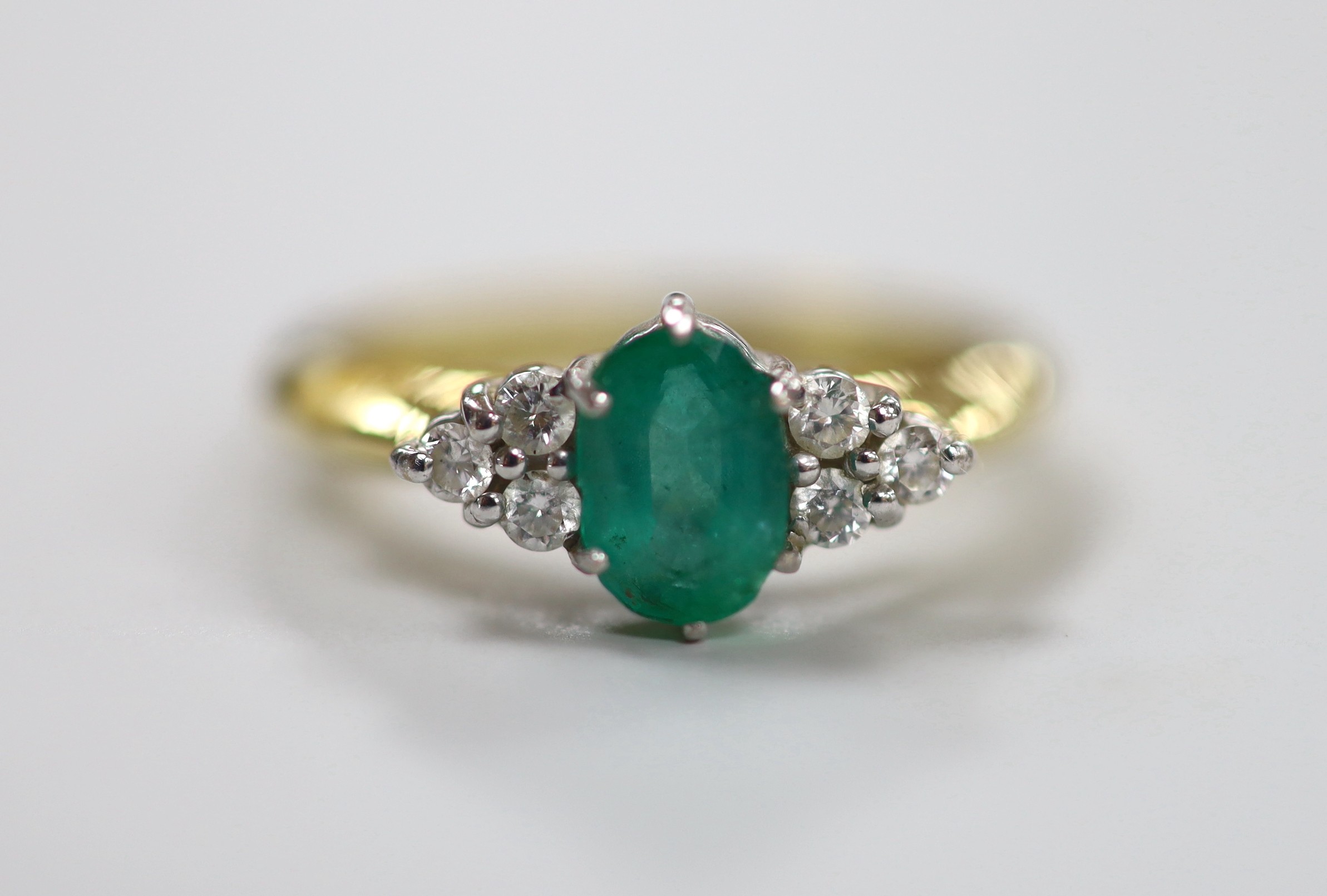 A modern 18ct gold and single stone oval cut emerald set ring, with six stone diamond chip set shoulders, size N/O, gross weight 4.8 grams.